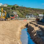 A large construction site featuring a bulldozer and a truck, showcasing civil engineering work on a beach.