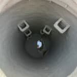 Top-down perspective of a deep, round manhole that has been successfully sprayed with light-grey grouting. This seals the manhole from infiltration and exfiltration.